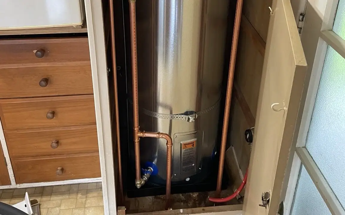 Base of a mains pressure hot water cylinder in a cupboard, showing the safe tray, drain valve and pipework