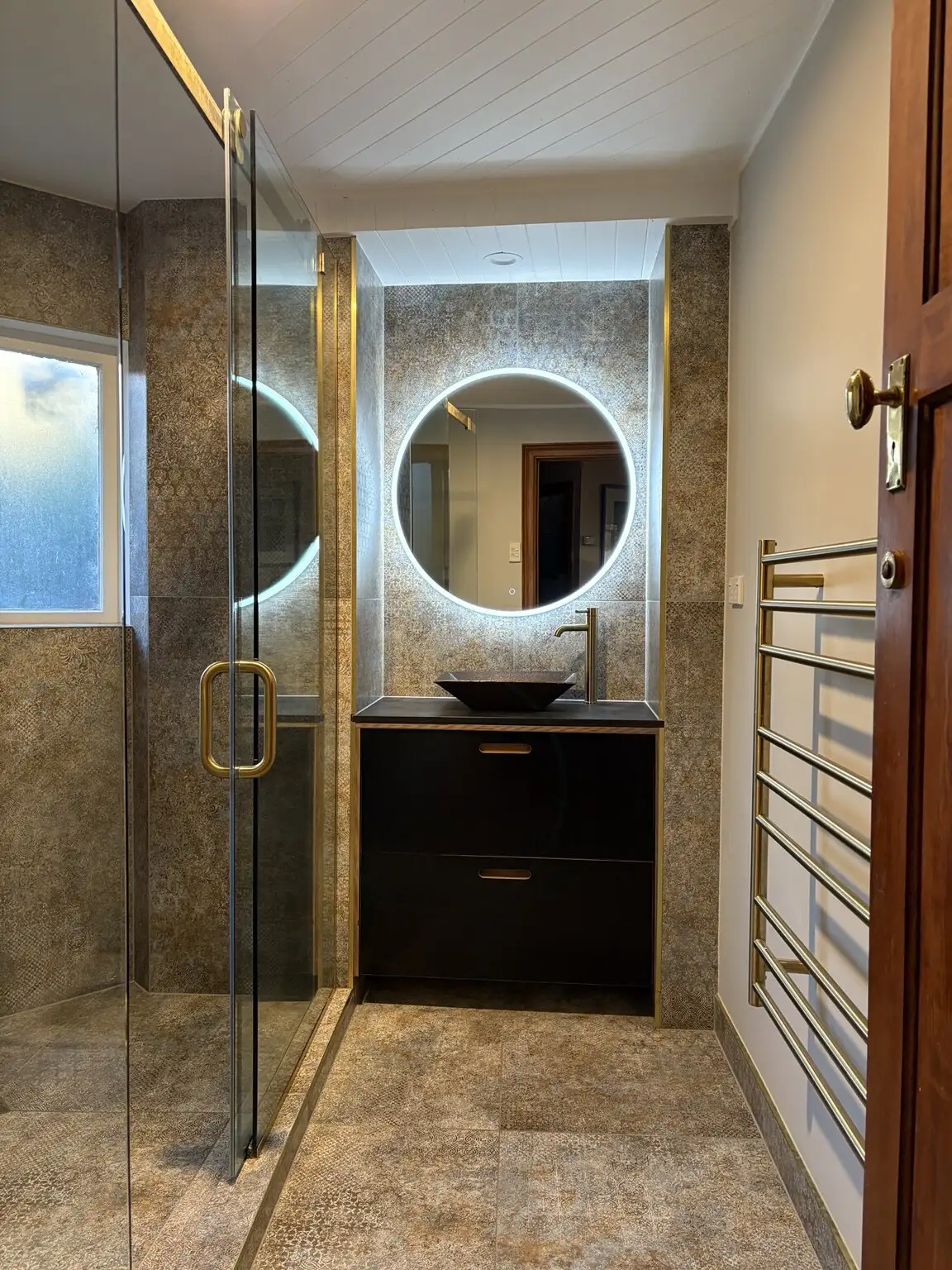 Finished dark-tiled bathroom with LED mirror and brass tapware